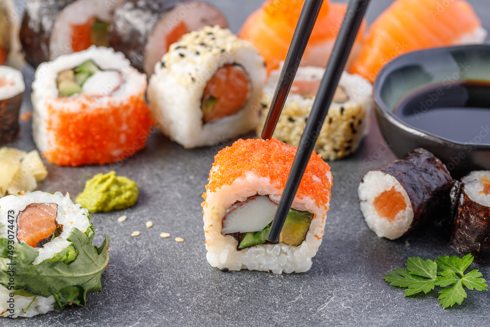 寿司配鳄梨、鱼糜和刺山柑鱼子酱，用筷子夹在石板上。