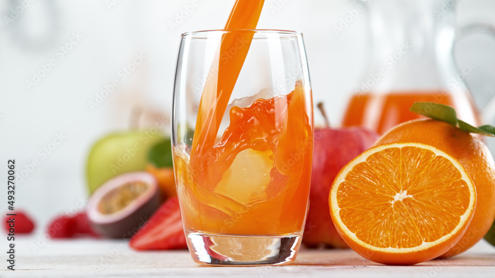多种维生素果汁倒入玻璃杯。厨房里有新鲜的橙汁和桔子水果。