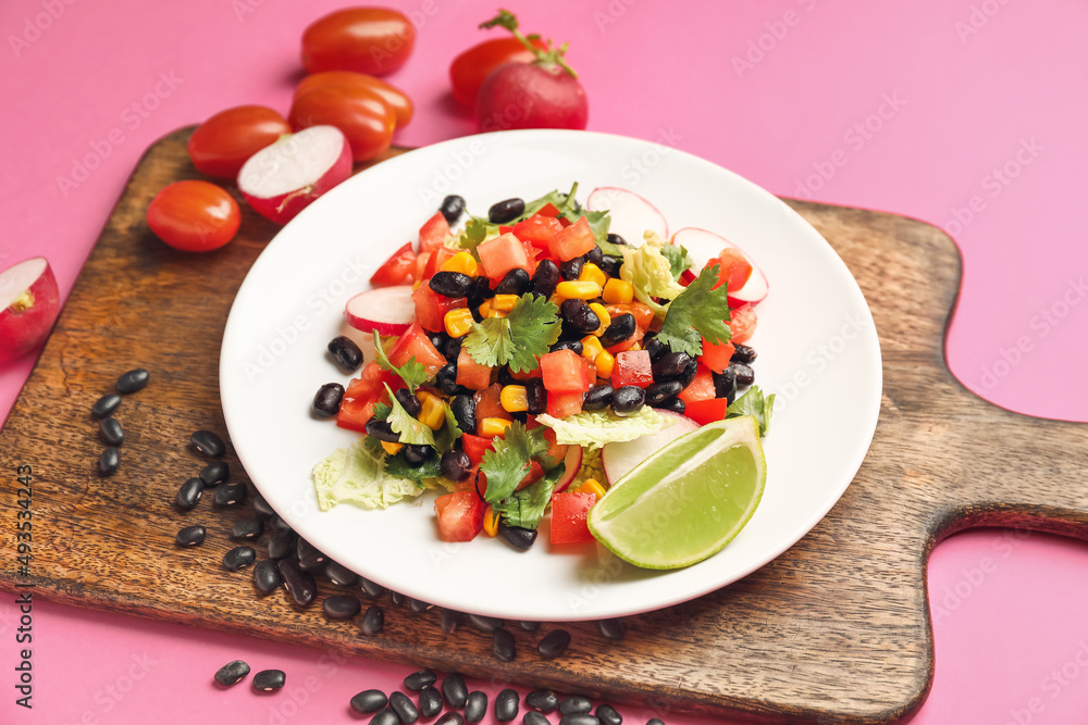 Wooden board with plate of tasty Mexican vegetable salad on pink background, closeup
