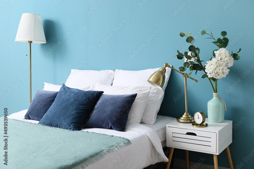 舒适的床，床头柜桌上的花瓶和蓝色墙壁附近的现代灯