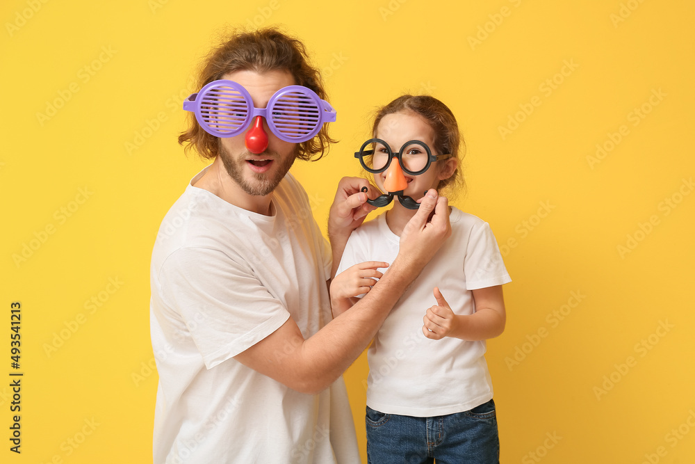 有趣的男人和她的小女儿在黄色背景下伪装。愚人节庆祝活动