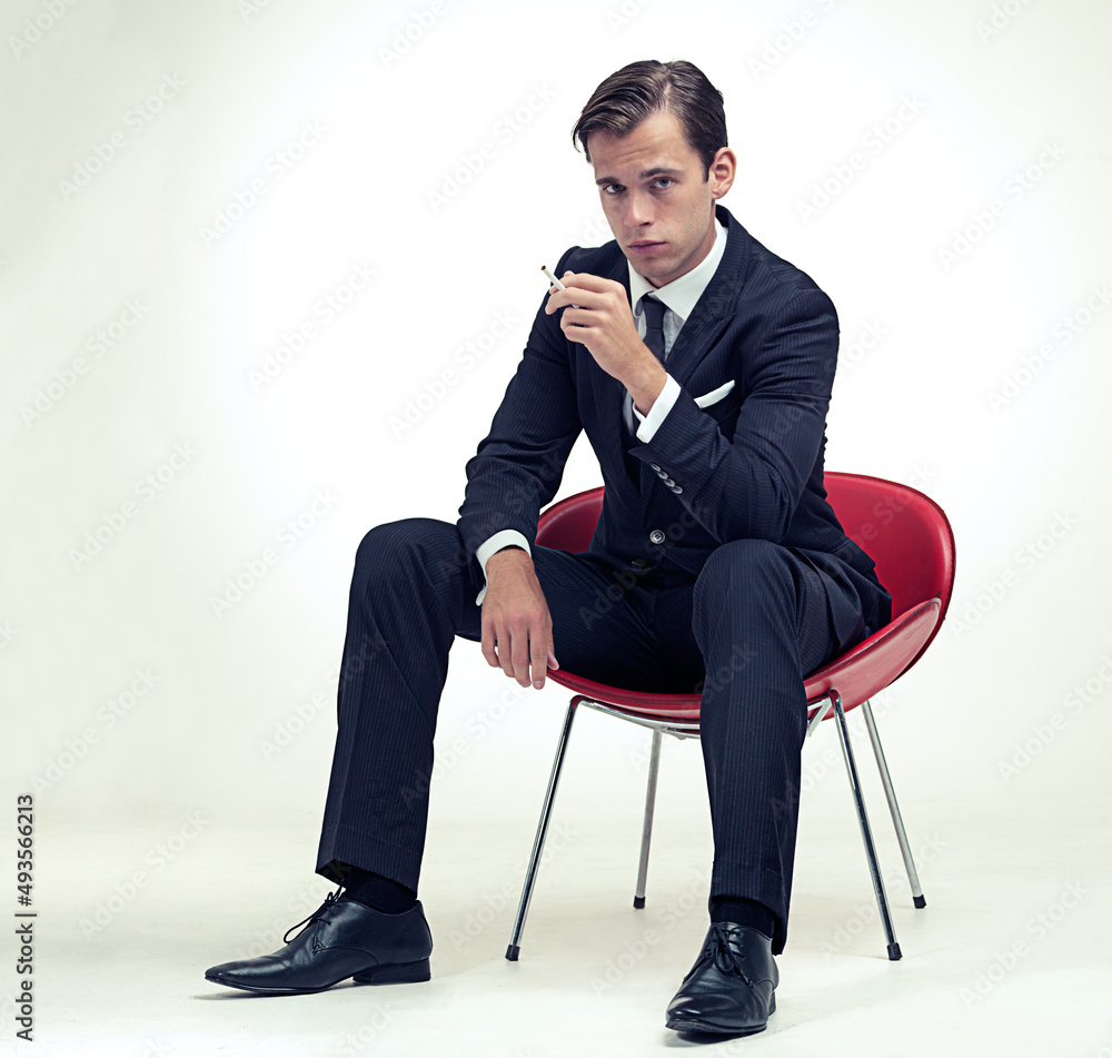 优雅的吸烟者。一幅工作室肖像，画中一位身穿细条纹西装的英俊年轻绅士坐在椅子上