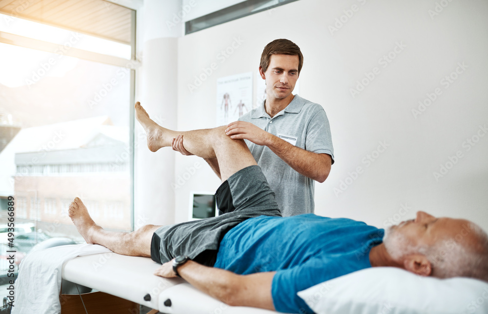 客户的健康是他唯一关心的问题。一位年轻的男性理疗师帮助一位腿部康复患者的照片