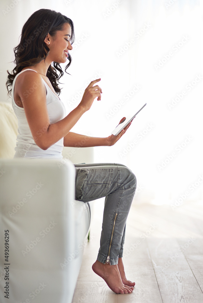 今天要浏览什么。一张年轻女子在家沙发上放松时使用平板电脑的照片。