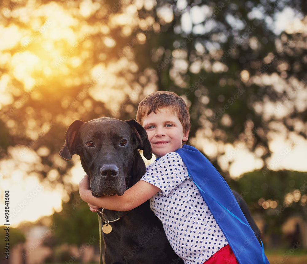 每个超级英雄都需要一只超级狗。一个小男孩和他的狗在玩耍时戴着斗篷的照片