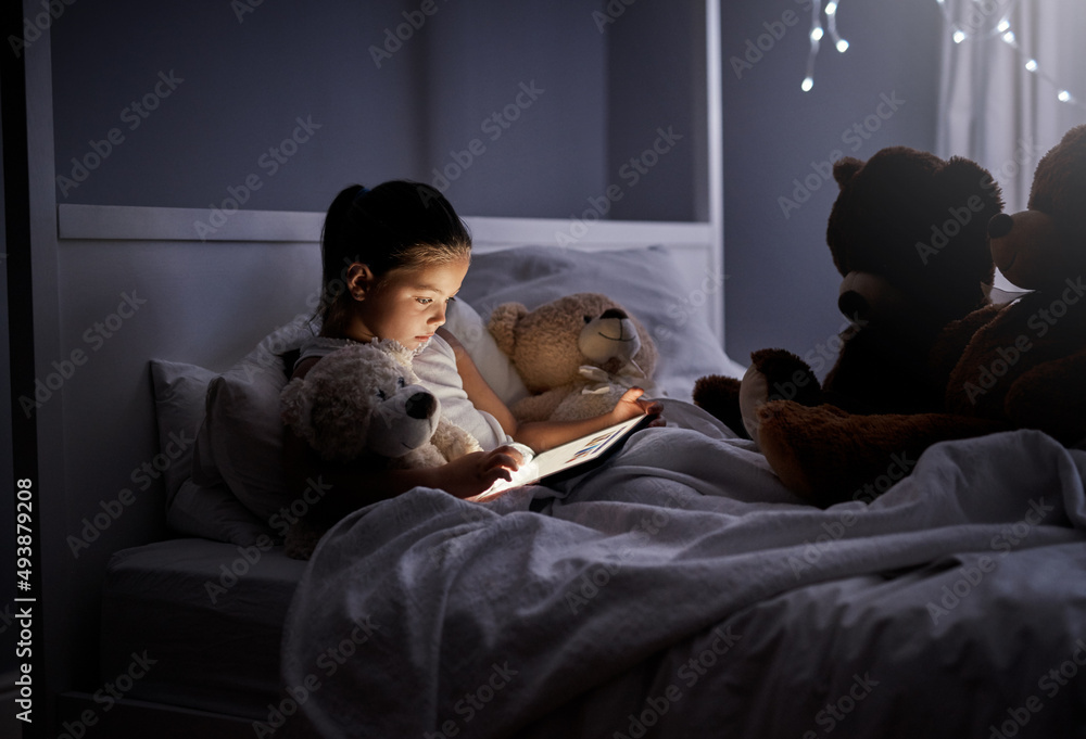 这些乏味的人需要他们的睡前故事。一个可爱的小女孩在床上使用数字平板电脑的照片