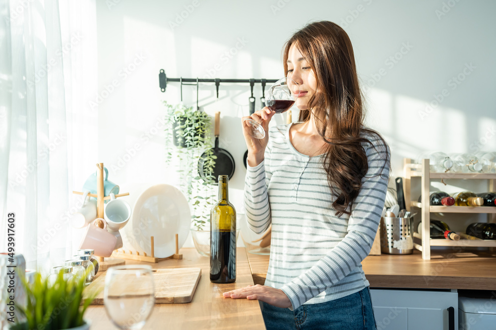 一位有魅力的亚洲年轻女子在家里的厨房里用玻璃杯喝酒。