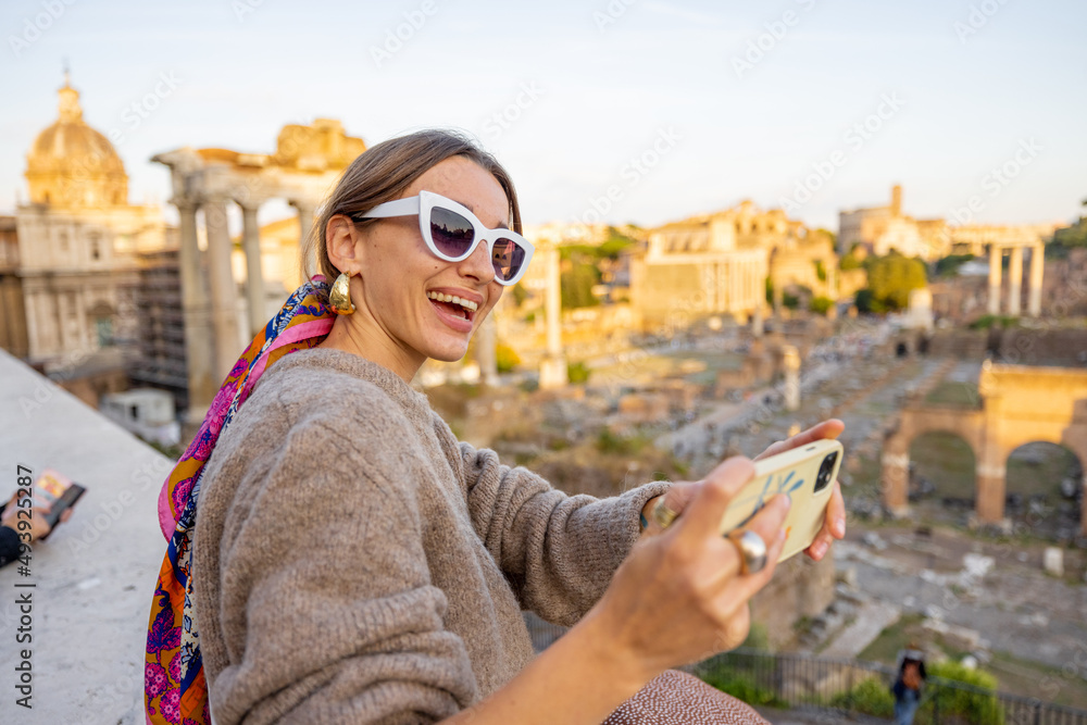 Woman takes selfie photo on background of the Roman Forum, ruins at the center of Rome on a sunset. 