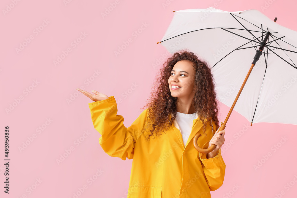 身穿黄色雨衣、粉色背景带伞的年轻非裔美国妇女