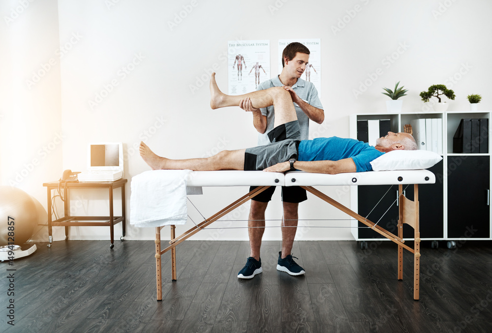 我们一步一个脚印。一位年轻的男性理疗师帮助一位客户锻炼腿部的照片