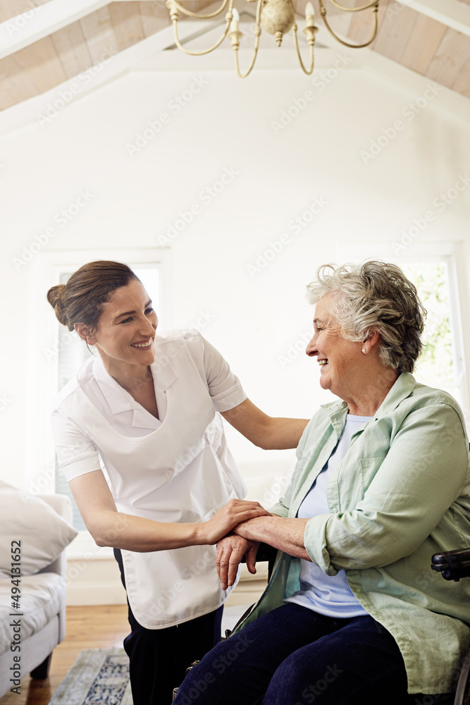 确保她得到很好的照顾。一位面带微笑的护理人员帮助一位坐在轮椅上的老年妇女的照片