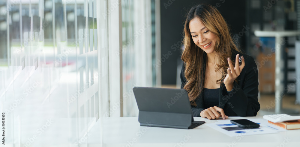 快乐的年轻亚洲女性坐在办公桌前，用笔记本电脑进行视频通话
