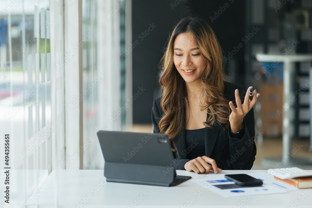 Happy young Asian woman sitting at desk at work and using laptop computer for video call