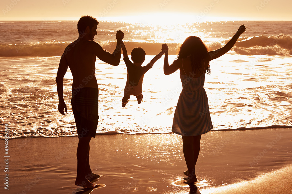 一个幸福的家庭。一对夫妇在海滩上散步时在他们之间摇摆孩子的后视图