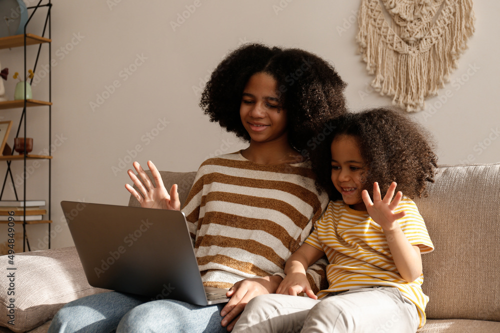 两个不同年龄的漂亮黑人女孩在家里视频通话。亲爱的姐妹坐在一起