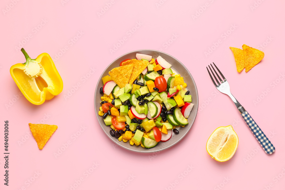 盘子里有墨西哥蔬菜沙拉、玉米片、甜椒和柠檬，背景为粉色