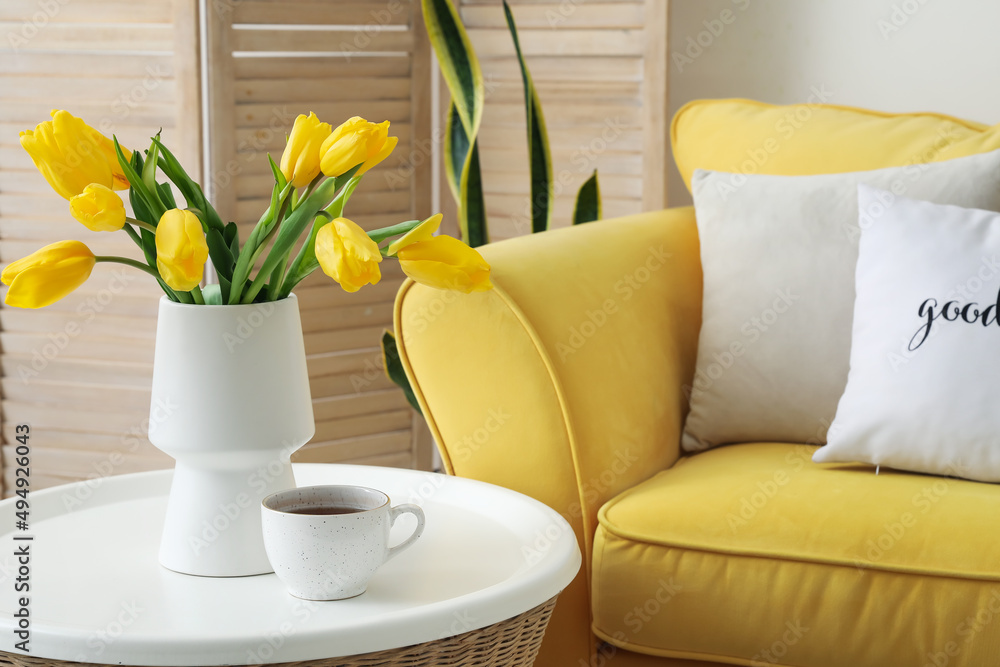 Vase with yellow tulips and cup of coffee on table in living room