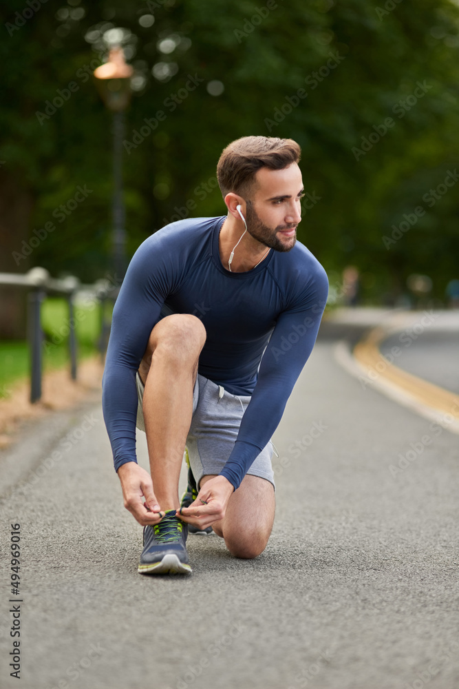Laced up and ready to go. Full length shot of a handsome young male runner tying his shoelaces durin