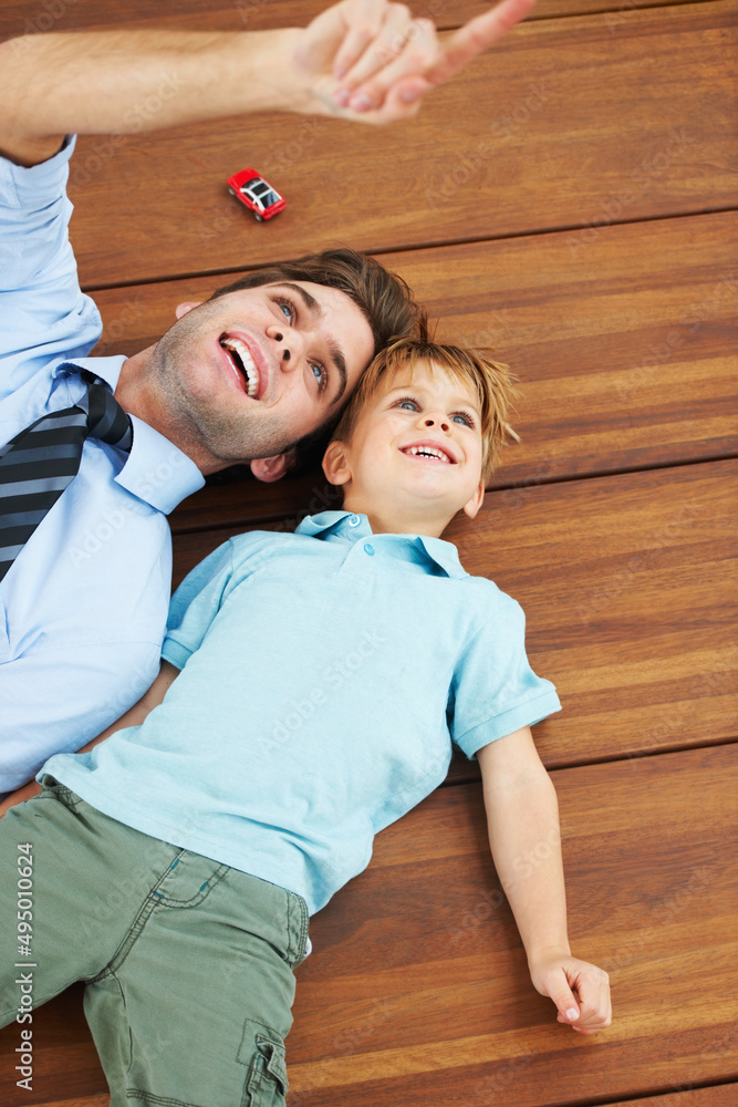 看那边。一个可爱的男孩和他年轻的父亲躺在地板上，抬头看着什么。