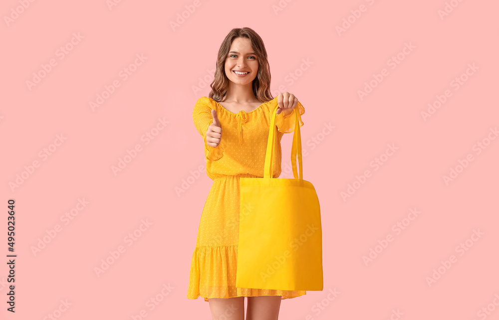 漂亮的年轻女子，黄色环保袋，粉色背景上竖起大拇指
