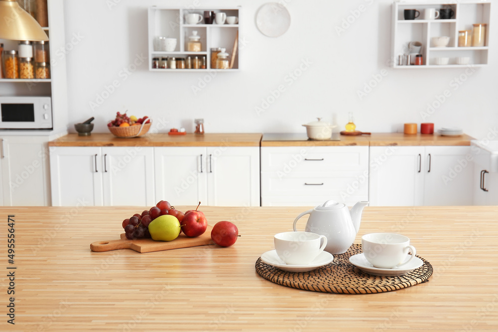 厨房餐桌上有杯子、盘子和水果的茶壶