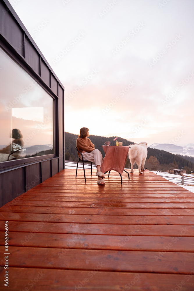 一个女人带着她的狗在山里一所小房子的露台上休息，欣赏美丽的风景d