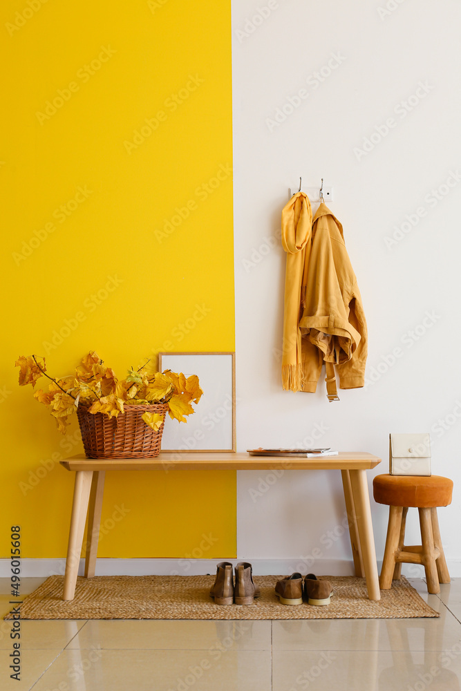 走廊彩色墙附近桌子上有秋天的叶子和空白框架的篮子