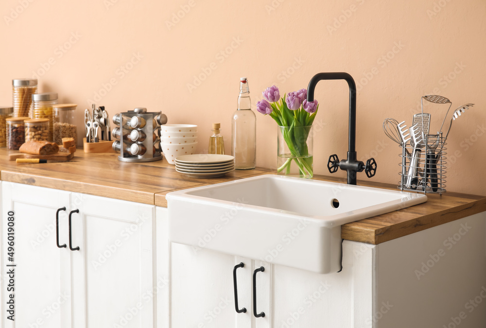 带水槽的白色柜台、花瓶里的郁金香和米色墙壁附近的厨房用具