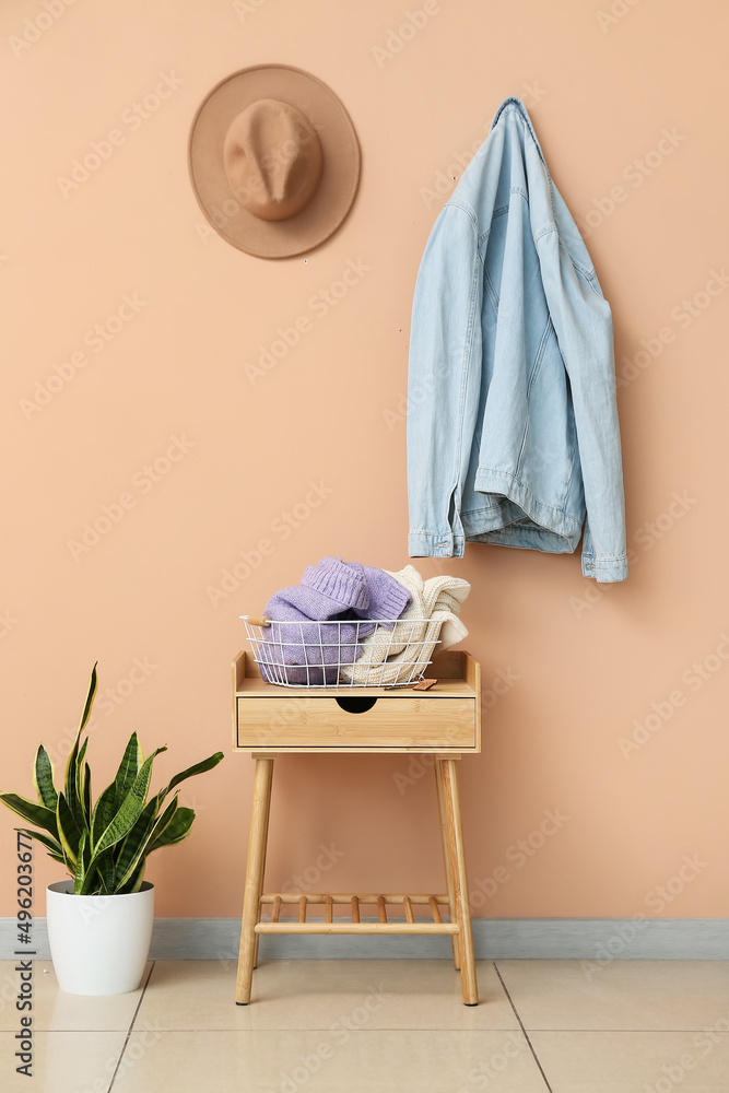 桌子上放着针织毛衣的篮子，大厅米色墙壁附近的室内植物