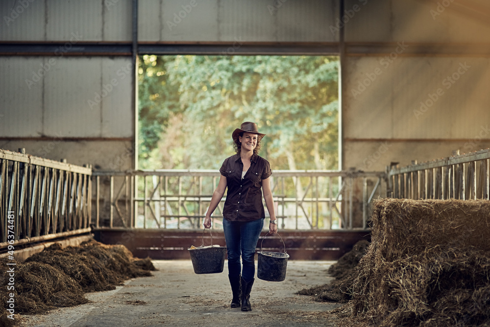 实现梦想。一个快乐的女农民提着水桶走出谷仓的镜头。