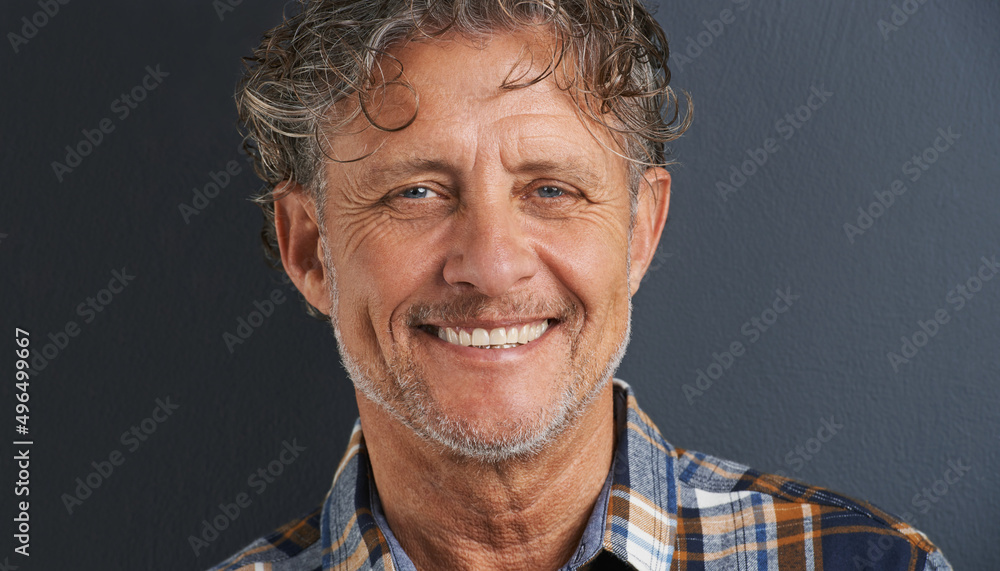 一个英俊的微笑。灰色背景下，一个快乐成熟的男人的裁剪肖像。