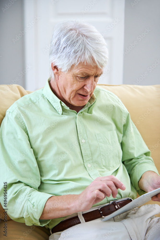在网上寻找答案。一位老人坐在沙发上使用数字平板电脑的照片