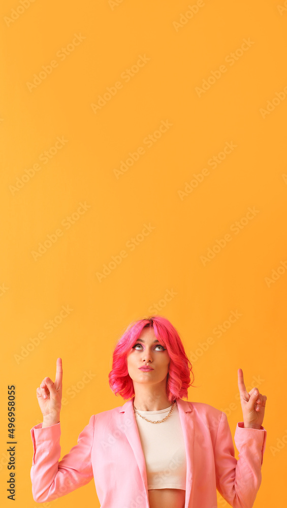 一头亮粉色头发的时髦女人指着黄色背景上的东西