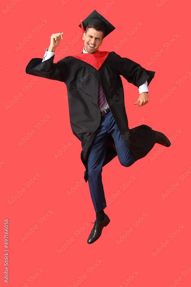 年轻的男毕业生在红底上跳跃