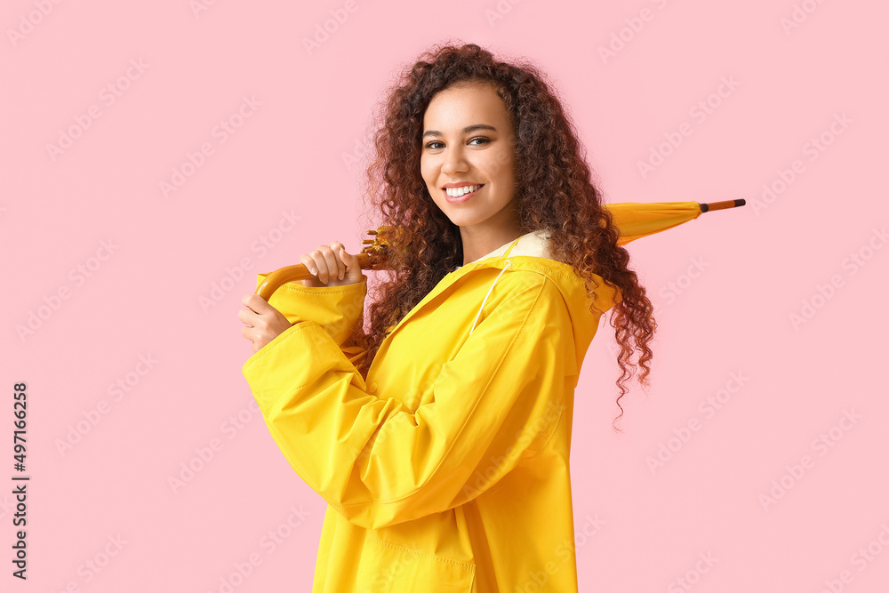 身穿黄色雨衣、粉色背景带伞的年轻非裔美国妇女