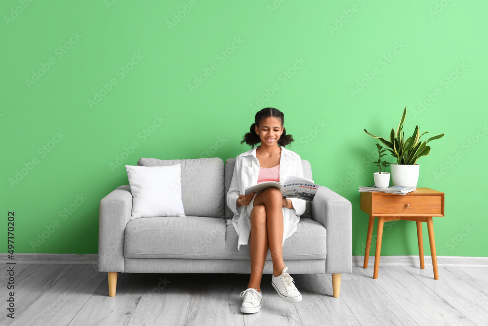 非裔美国少女坐在家里的沙发上看杂志