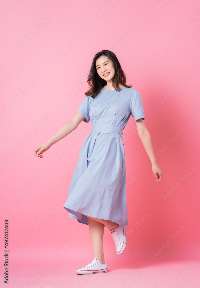 身穿粉色背景蓝色连衣裙的年轻亚洲女性的全长照片
