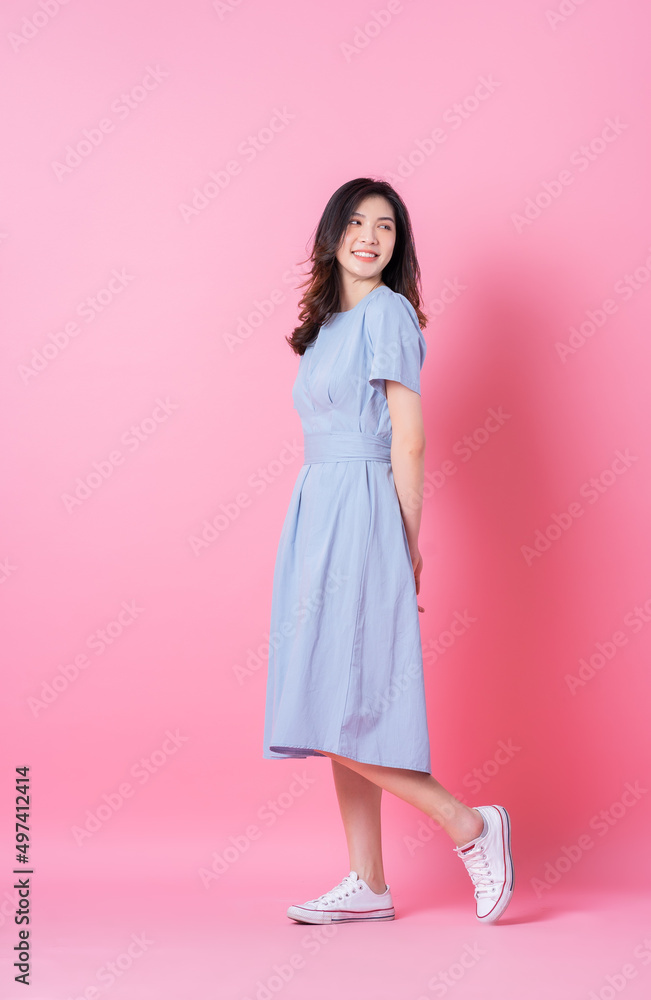 粉色背景下身穿蓝色连衣裙的年轻亚洲女性的全长照片
