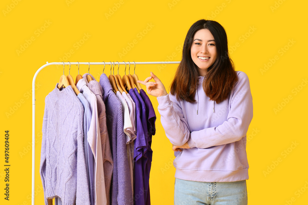 年轻的亚洲女人指着货架，黄色背景上有紫色的衣服