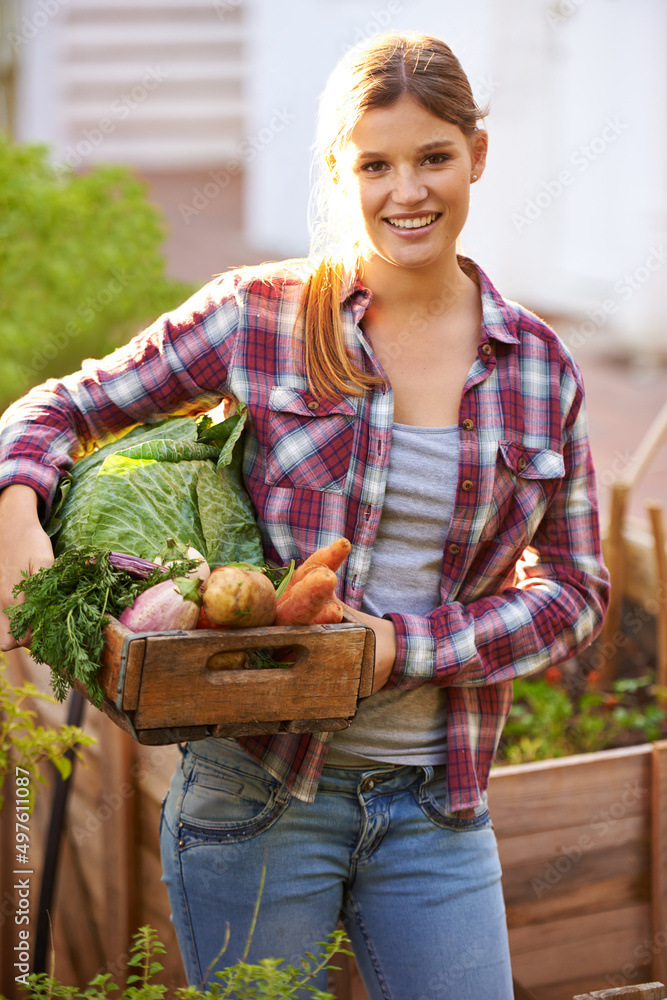 你变绿了吗？一个快乐的年轻女人拿着一箱新鲜采摘的蔬菜的画像