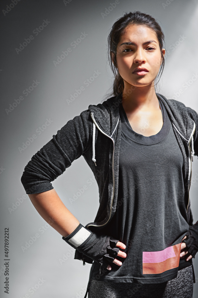 专注于健身。一位穿着运动服的健康年轻女性在灰色背景下摆姿势的肖像