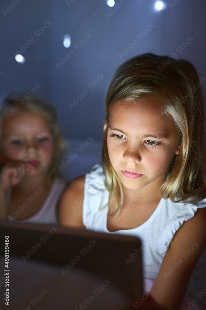 应用时代的就寝时间。两个小女孩睡前使用数字平板电脑的镜头。