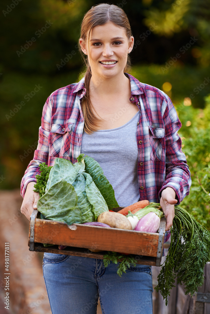 只有有机的。一个快乐的年轻女人拿着一箱新鲜采摘的蔬菜的画像。