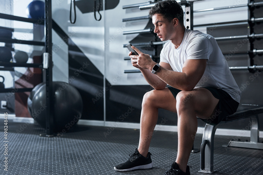 查看最新的健身应用程序。一张运动型年轻人在健身房使用手机的照片。