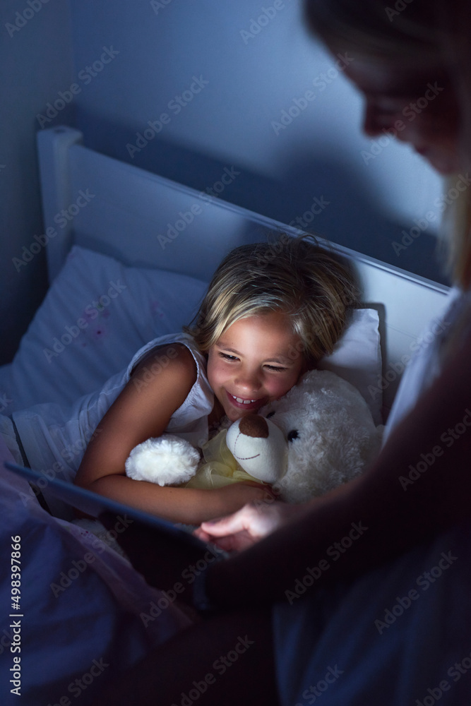 数字时代的故事时间。一个小女孩和她的母亲在睡前使用数字平板电脑的镜头