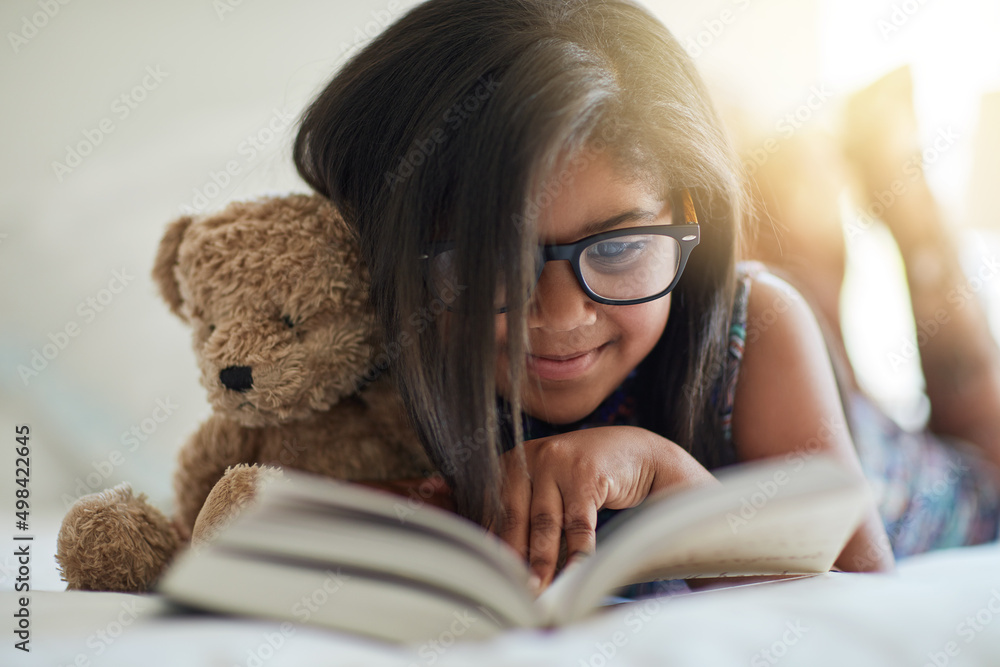 我们喜欢讲故事的时间，任何时候。一个可爱的小女孩和她的泰迪熊在卧室看书的镜头