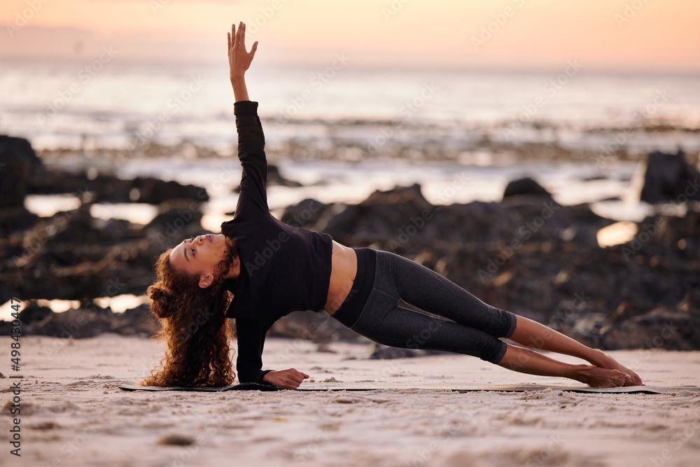 每个体式都要呼吸。日落时分，一位迷人的年轻女子独自在海滩上做瑜伽的照片