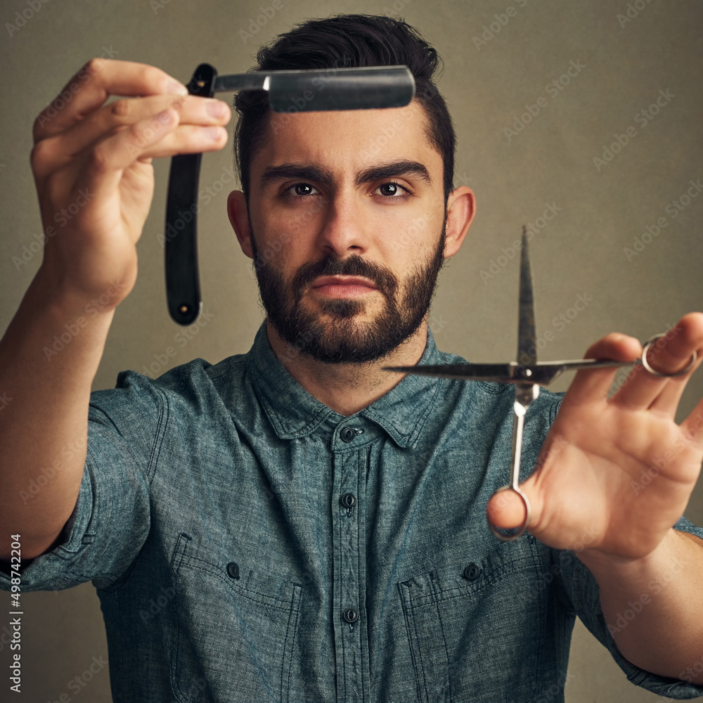 修剪是的，剃不是。工作室拍摄的一个英俊的年轻人手里拿着一把直剃刀和一把剪刀