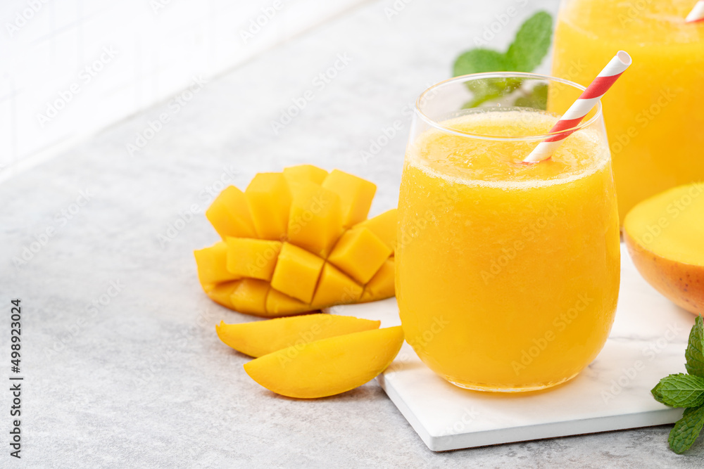 新鲜美味的芒果汁奶昔，装在灰色桌子背景的玻璃杯里。