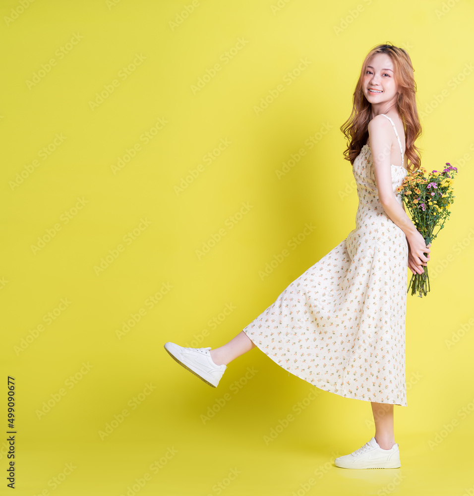 黄色背景下年轻的亚洲女子手捧鲜花的形象